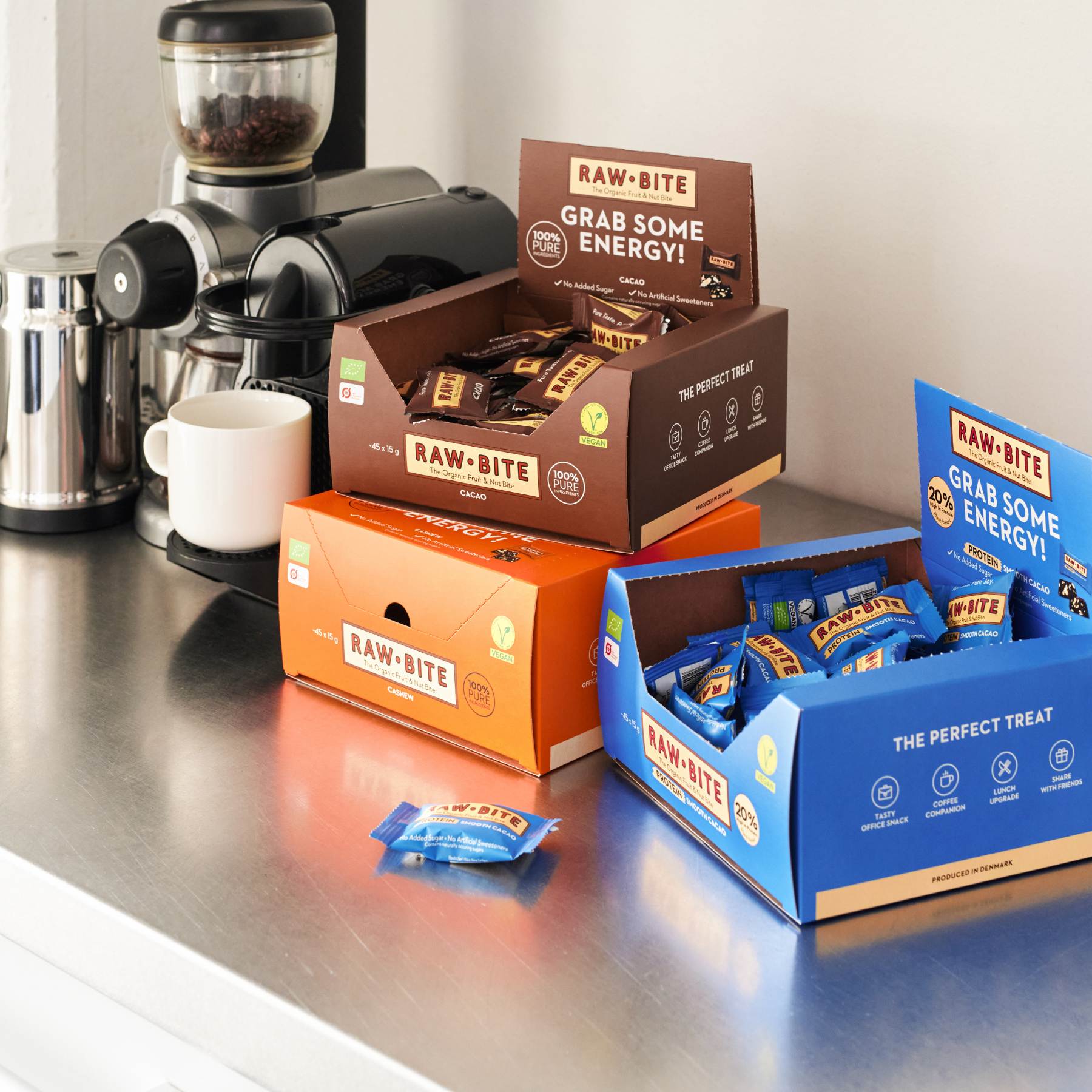 RAWBITE mini bars in various packaging on a kitchen counter with a coffee grinder and mug.
