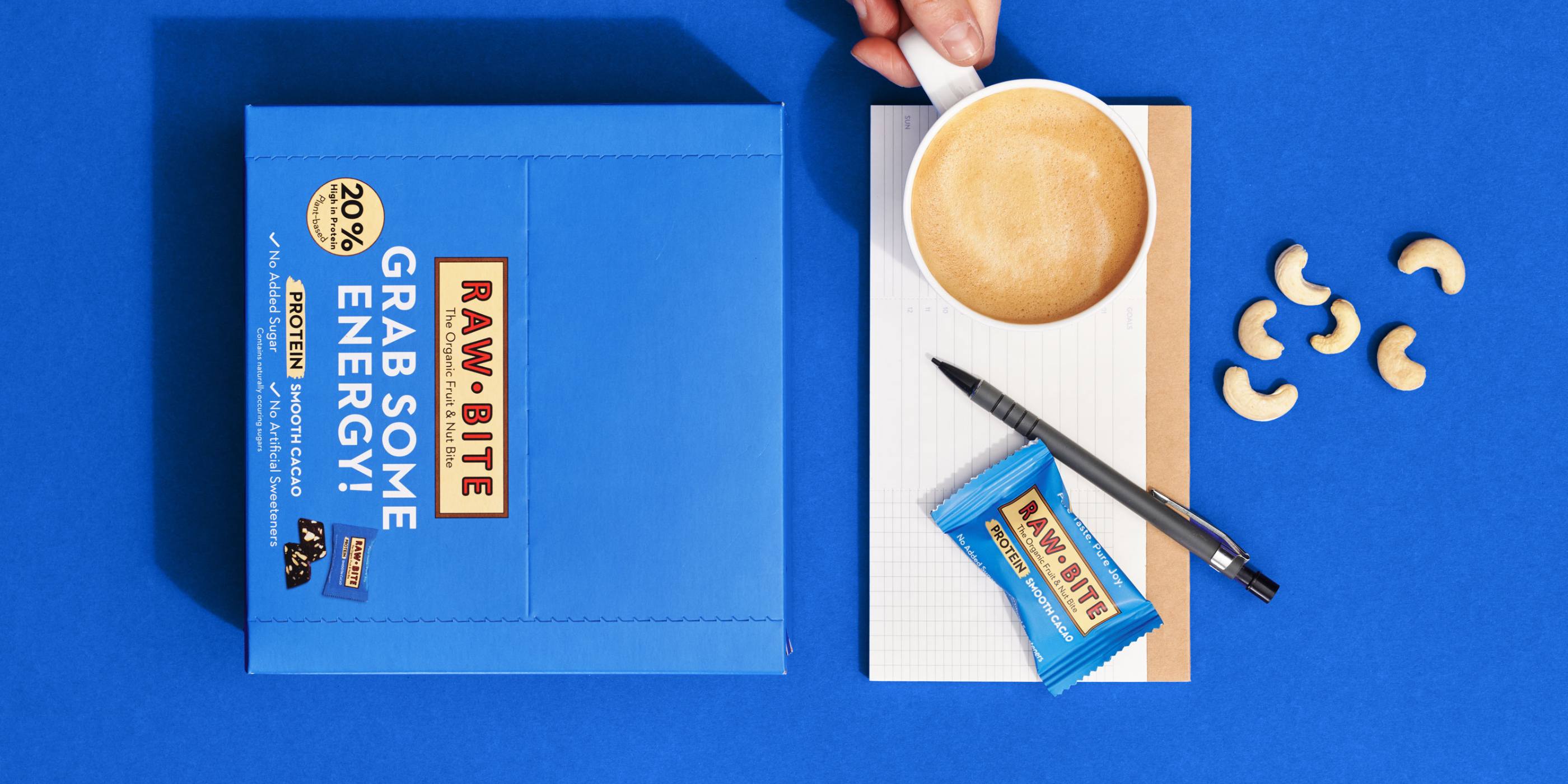 RAWBITE Protein Smooth Cacao Office Box with a cup of coffee and snack on a blue background