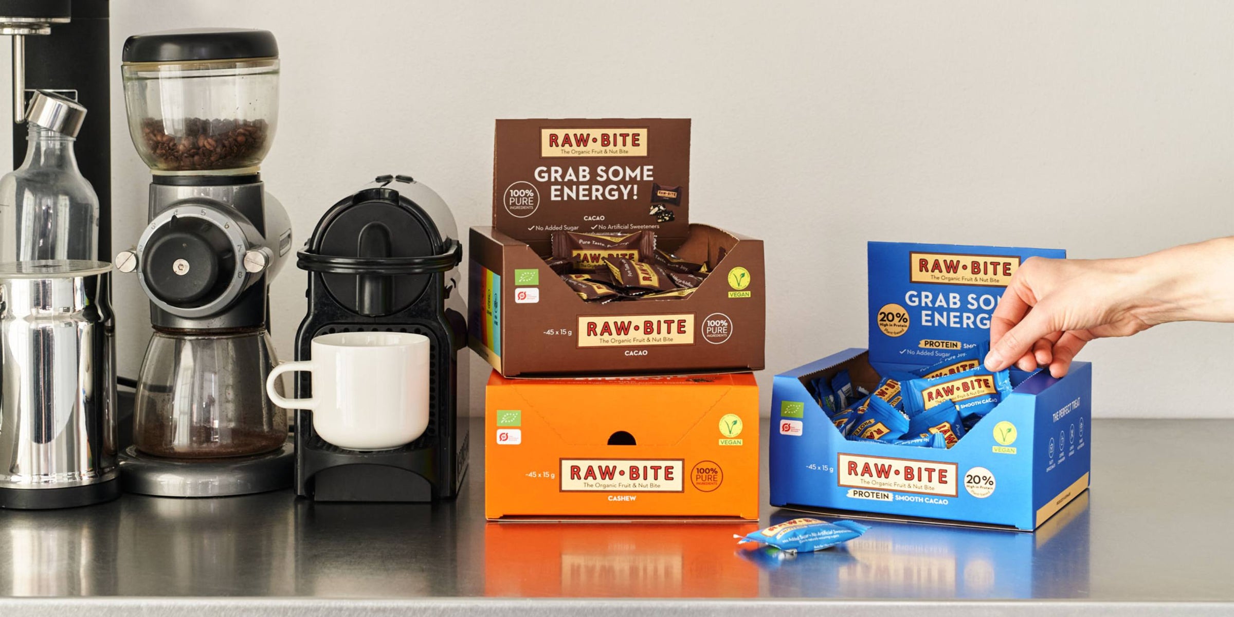 RAWBITE Office Boxes displayed on a counter with coffee-making equipment.