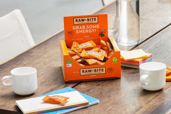 Box of RAWBITE cashew mini bars on a table with mugs and snacks.
